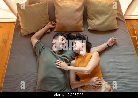 Giovane coppia riposante sdraiata sul letto con tre cuscini durante la vacanza estiva Foto Stock