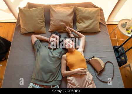Giovane coppia di viaggiatori contemporanei che tengono per mano mentre si sdraia sul letto in una casa glamping Foto Stock