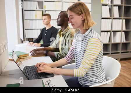 Vista laterale su un gruppo di studenti incluso con un giovane uomo che legge un libro in braille in biblioteca Foto Stock