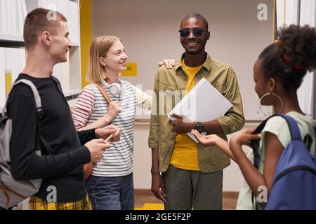 Ritratto in vita di diversi gruppi di studenti che chiacchierano con un uomo cieco sorridente Foto Stock