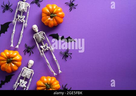 Buon concetto di vacanza di Halloween. Composizione piatta con scheletri spaventosi, zucche, ragni, silhouette a pipistrello su sfondo viola. Vista dall'alto, vista dall'alto Foto Stock