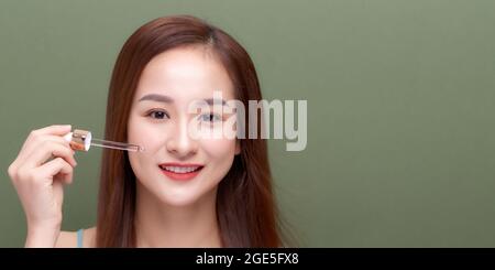 Bella giovane donna che applica siero sulla sua pelle contro sfondo di colore Foto Stock