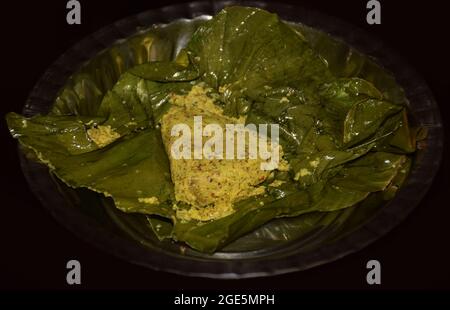 Mano di una donna che copre una bistecca di pesce coperta con olio di senape e semi di papavero con foglia di banana Foto Stock