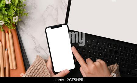 Elegante spazio di lavoro femminile con le mani femminili che utilizzano il mockup dello smartphone durante il lavoro su tablet, schermo vuoto del dispositivo, pullover in maglia, modern dec Foto Stock