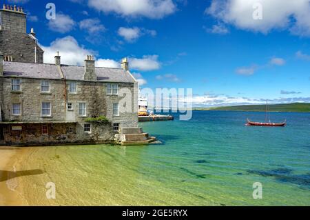 Baia tranquilla con acqua cristallina, porto, casa di pietra e nave vichinga, Lerwick, Isole Shetland, Scozia, Regno Unito Foto Stock