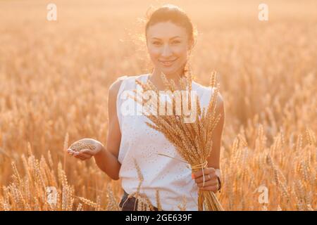 Donna che tiene covone di spighe di grano a campo agricolo. Foto Stock