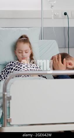 Ricoverata figlia malata che dorme dopo aver subito un intervento medico mentre il padre preoccupato pregava per il recupero della salute. Bambino con tubo nasale che riposa nel letto durante l'esame di malattia nel reparto ospedaliero Foto Stock