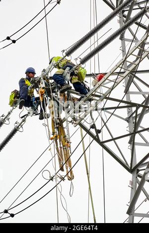 Uomini che lavorano in quota, ristrutturando i piloni elettrici, Inghilterra settentrionale, Regno Unito Foto Stock