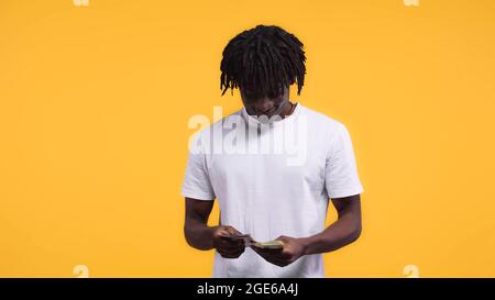 felice uomo afroamericano contando dollari isolati sul giallo Foto Stock