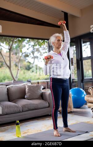 Donna caucasica anziana in soggiorno esercitandosi, alzandosi e sollevando manubri Foto Stock