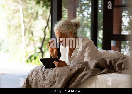 Donna caucasica anziana sdraiata sul male e facendo videochiamata Foto Stock