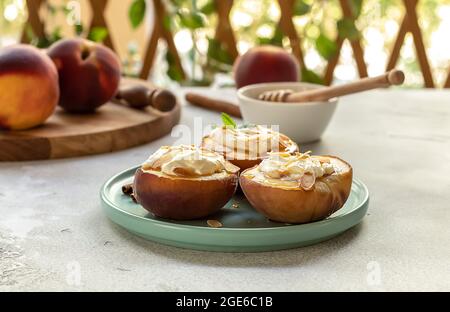 Pesche al forno con cannella, petali di mandorle, formaggio cremoso e miele su un fondo di cemento chiaro. Frutta in un piatto con menta, vista dall'alto, spazio di copia. Foto Stock