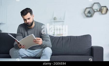 uomo insoddisfatto che guarda la cartella mentre si siede sul divano nel soggiorno Foto Stock