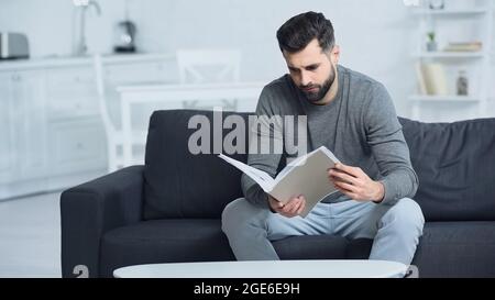 uomo stressato che guarda la cartella mentre si siede sul divano Foto Stock