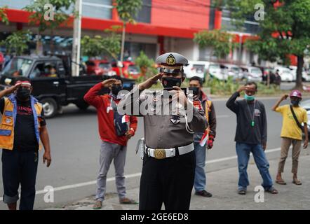 Makassar, Indonesia, 17 agosto 2021. Un poliziotto di Makassar celebra il 76° giorno dell'Indipendenza indonesiana in modo unico. Questo poliziotto ha invitato gli addetti al parcheggio a svolgere la cerimonia praticamente mentre si guarda un telefono cellulare che stava trasmettendo una trasmissione in diretta della cerimonia della bandiera al Palazzo di Stato. Credit: Herwin Bahar/Alamy Live News Foto Stock