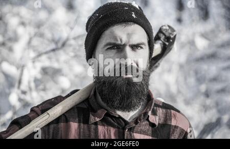 Lumberjack nel bosco con un'ascia. Brutale uomo con barba e baffi durante la giornata invernale, foresta innevata. Bell'uomo, hipster, lumberjack. Foto Stock