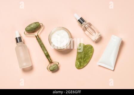 Prodotti cosmetici - Jade Roller e massaggiatore gua sha con bottiglie per panna e siero. Foto Stock