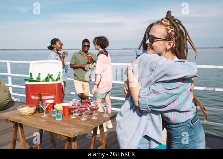 Bella giovane donna con Dreadlock abbracciare amico quando frequenta la sua festa di compleanno sul molo Foto Stock