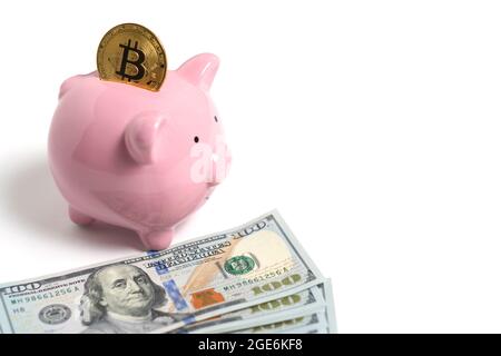 Bitcoin Piggy banca e pacchetto di centinaia di dollari bollette sparse su sfondo bianco. Foto Stock