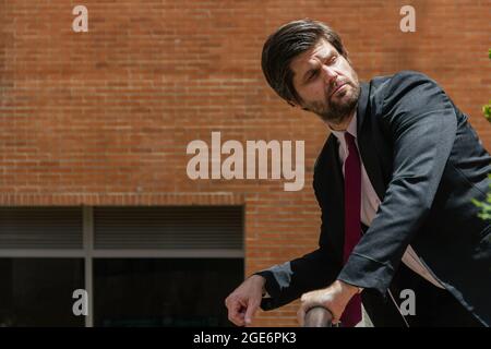 uomo elegante che indossa un vestito nero e una cravatta rossa appoggiata alla ringhiera Foto Stock