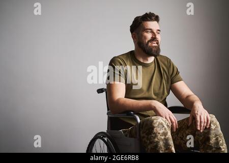 Ufficiale sorridente che indossa un uniforme e si siede su una sedia a rotelle Foto Stock