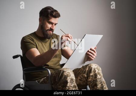 Ex-serviceman seduto su una sedia a rotelle e dipingere una foto su una tela Foto Stock
