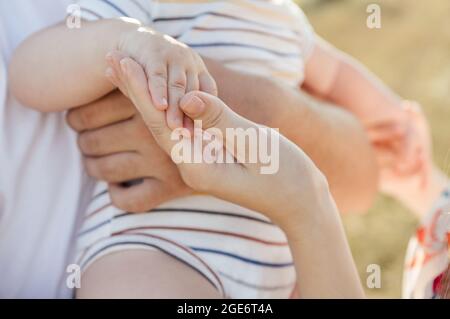 Primo piano foto delle mani della giovane famiglia con il bambino che lo tiene e si prende cura di lui Foto Stock