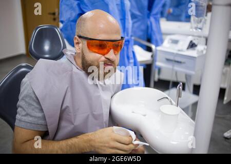 Il maschio caucasico sta lavando la sua bocca durante un'operazione di estrazione del dente di saggezza in un ospedale dentale. Foto Stock