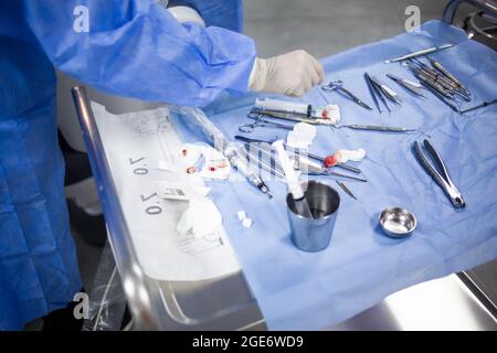 Un chirurgo sta prendendo uno strumento medico da una tavola di vassoio con gli attrezzi dentali, le medicine e l'apparecchiatura durante un ambulatorio dei denti Foto Stock