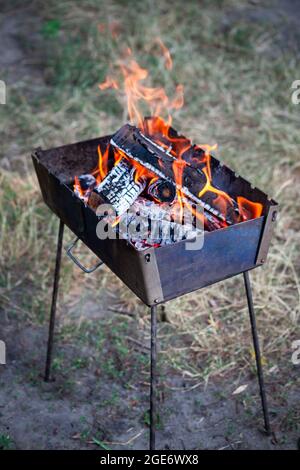 Un piccolo braciere pieghevole portatile riempito di legno in fiamme. Cottura  sulla griglia. Fuoco sicuro in natura. Legna da ardere. Fiamme in braciere  Foto stock - Alamy