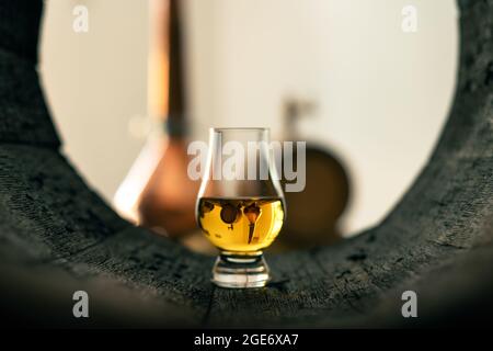Un bicchiere di whisky in un vecchio barile di quercia. Rame alambic sullo sfondo. Tradizionale concetto di distilleria alcolica Foto Stock