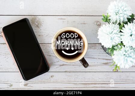 Buon saluto del mattino con una tazza di caffè con smartphone e fiore Foto Stock
