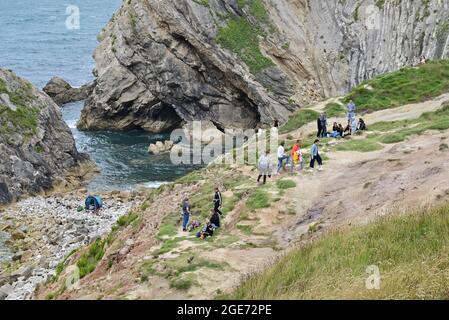 Persone sulle rocce a Stair Hole, Lulworth Cove, Dorset, Regno Unito, 17 agosto 2021, Meteo. L'estate continua in una vena fredda e deludente, ma le nuvole alla fine danno il posto al sole luminoso sulla Costa Giurassica. Credit: Paul Biggins/Alamy Live News Foto Stock
