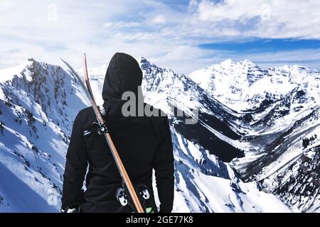 Persona con cappuccio con sci sul retro in cima al concetto di sci estremo di montagna invernale Foto Stock