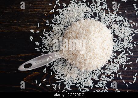 Una coppa di misurazione piena di riso a grani lunghi non cotti: Una coppa di misurazione in acciaio inox riempita con grani di riso bianco crudo Foto Stock