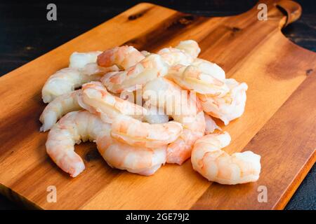 Gamberetti grezzi su un tagliere di legno: Gamberetti sbucciati e sbucciati non cotti su un tagliere di legno Foto Stock