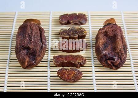 Presentazione di diversi hoshigaki su un tappeto di bambù su un tavolo, uno affettato accanto a due persimmon in stile giapponese essiccato Foto Stock