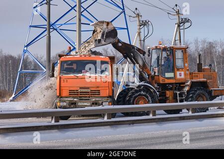 Rimozione della neve in inverno dalle strade con un escavatore e un veicolo KAMAZ camion - Mosca, Russia, 17 gennaio 2021 Foto Stock