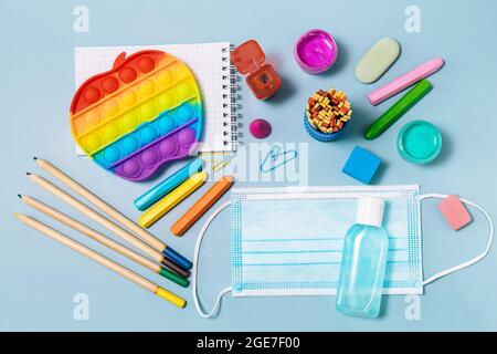 Forniture scolastiche, antipasto, maschera facciale, bottiglia di disinfettante, per il ritorno a scuola su sfondo blu. Precauzioni Covid-19. Vista dall'alto in piano Foto Stock