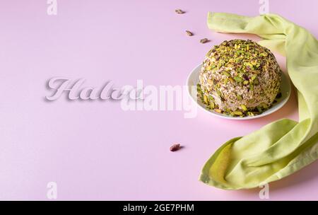 Halva di sesamo con pistacchi, poche noci disperse, tovagliolo di lino e testo Halva su carta rosa. Orientamento orizzontale. Dolce medio orientale tradizionale Foto Stock