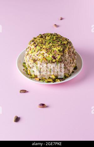 Pronto a mangiare halva di sesamo con pistacchi su piatto bianco e poche noci sparse su fondo di carta rosa. Dolci tradizionali mediorientali. Ebraico, t Foto Stock