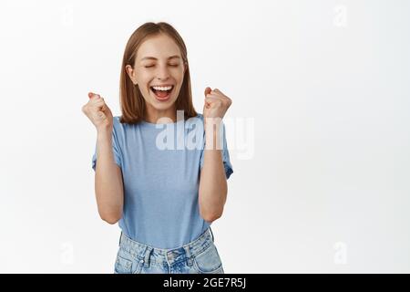 Sì, ha vinto. Felice giovane donna vincere premio e celebrare, fa pompa pugno e gridare dal piacere e dalla gioia, raggiungere obiettivo, trionfare, in piedi Foto Stock