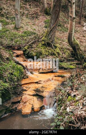 piccola cascata che scorre su una mensola di roccia arancione nei boschi Foto Stock