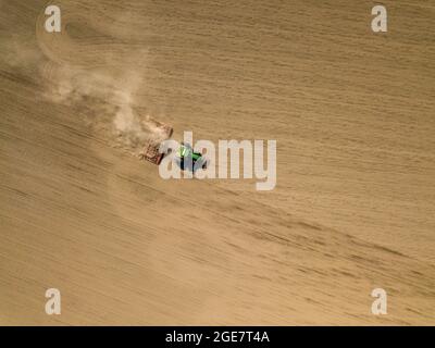 Vista aerea ad alto angolo del trattore verde che aratura un campo con terreno e polvere Foto Stock