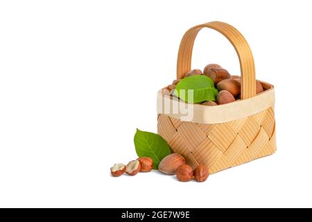 La nocciola si trova in un cestino di legno su uno sfondo bianco isolato. Nocciole non pelate in guscio e foglie verdi Foto Stock