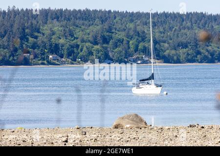 Una barca a vela con le sue vele abbassate ormeggiate nella baia in una giornata di sole Foto Stock