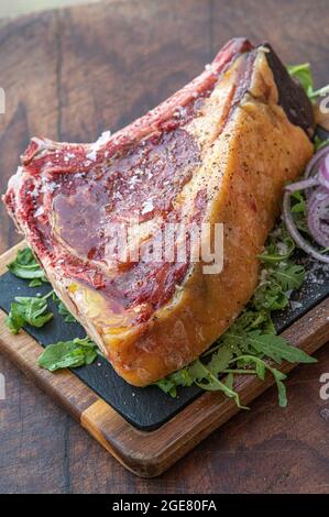 Deliziosa bistecca di manzo crudo di angus nero invecchiato pronta per essere cucinata su un tavolo di legno con cipolla e insalata di razzo Foto Stock