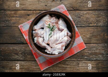 Le ali di pollo crude nel recipiente preparano per cucinare. Drumette fresche non cotte o drumstick con rosmarino per grigliare e barbecue su sfondo di legno. RAW Foto Stock