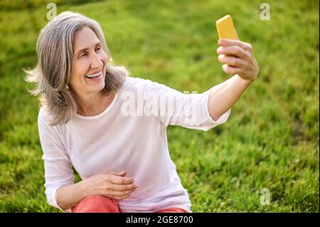 Donna adulta brillante con smartphone in mano estensibile Foto Stock