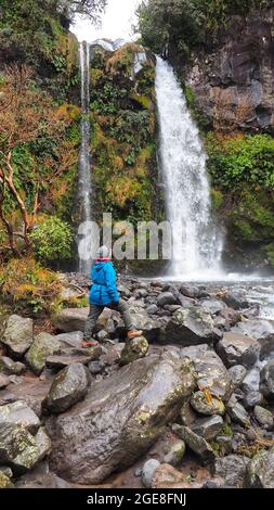 Un'escursionista di mezza età (62) alla base di Dawson Falls in pioggia, nel Parco Nazionale di Egmont, Nuova Zelanda Foto Stock